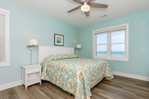 A bedroom with a bed, a nightstand, a ceiling fan, a window with a view of the ocean, and a framed picture on the wall. - Shellebration - Luxurious 8 BR, 8 BA Oceanfront Home - Pool & Elevator! (Surf City)