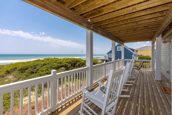 A wooden deck with white railings overlooking a beach and ocean.