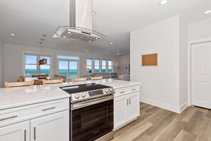 A modern kitchen with a large island, white cabinetry, and a view of the ocean.