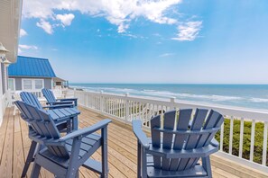 A wooden deck with Adirondack chairs overlooking a beach.
