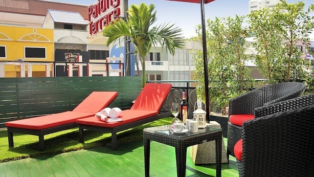 Un patio con dos sillones rojos, una mesa de mimbre con una botella, y una señalización que indica 'Palmy Place' al fondo.