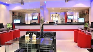 Una moderna zona de recepción con separadores de vidrio, asientos negros y rojos, y múltiples monitores.