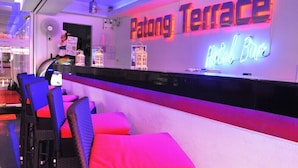 Zona de recepción de un hotel con un letrero de neón que dice 'Patong Terrace Hotel Bar'.