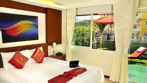 Una habitación de hotel con cama, escritorio con ordenador portátil, ventana con vistas al exterior y balcón con sombrilla roja.