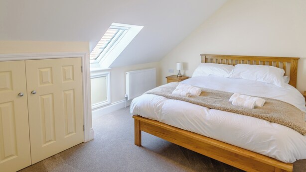 A bedroom with a sloped ceiling, a skylight, a bed with white linens, a wooden headboard, and a bedside table with a lamp. - Dawson Park 4 - UK12663 (Mablethorpe)