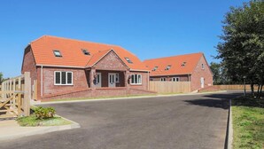 A two-story brick house with a red-tiled roof, a front porch, and a wooden fence. - Dawson Park 4 - UK12663 (Mablethorpe)