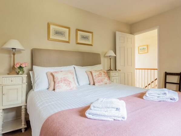 A neatly made bed with pillows, a bedside lamp, and a folded towel on a pink rug.