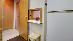 Casa de banho com porta de madeira, pia branca com espelho e um banquinho pequeno.