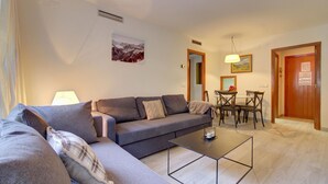 Uma sala de estar com um sofá cinzento, uma mesa de centro e um espaço de jantar com mesa e cadeiras.