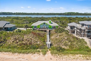 A beachfront property with a prominent house featuring a large balcony and a staircase leading to the beach. - Cloud Nine Home, Oceanfront with Game Room (Ponte Vedra Beach)
