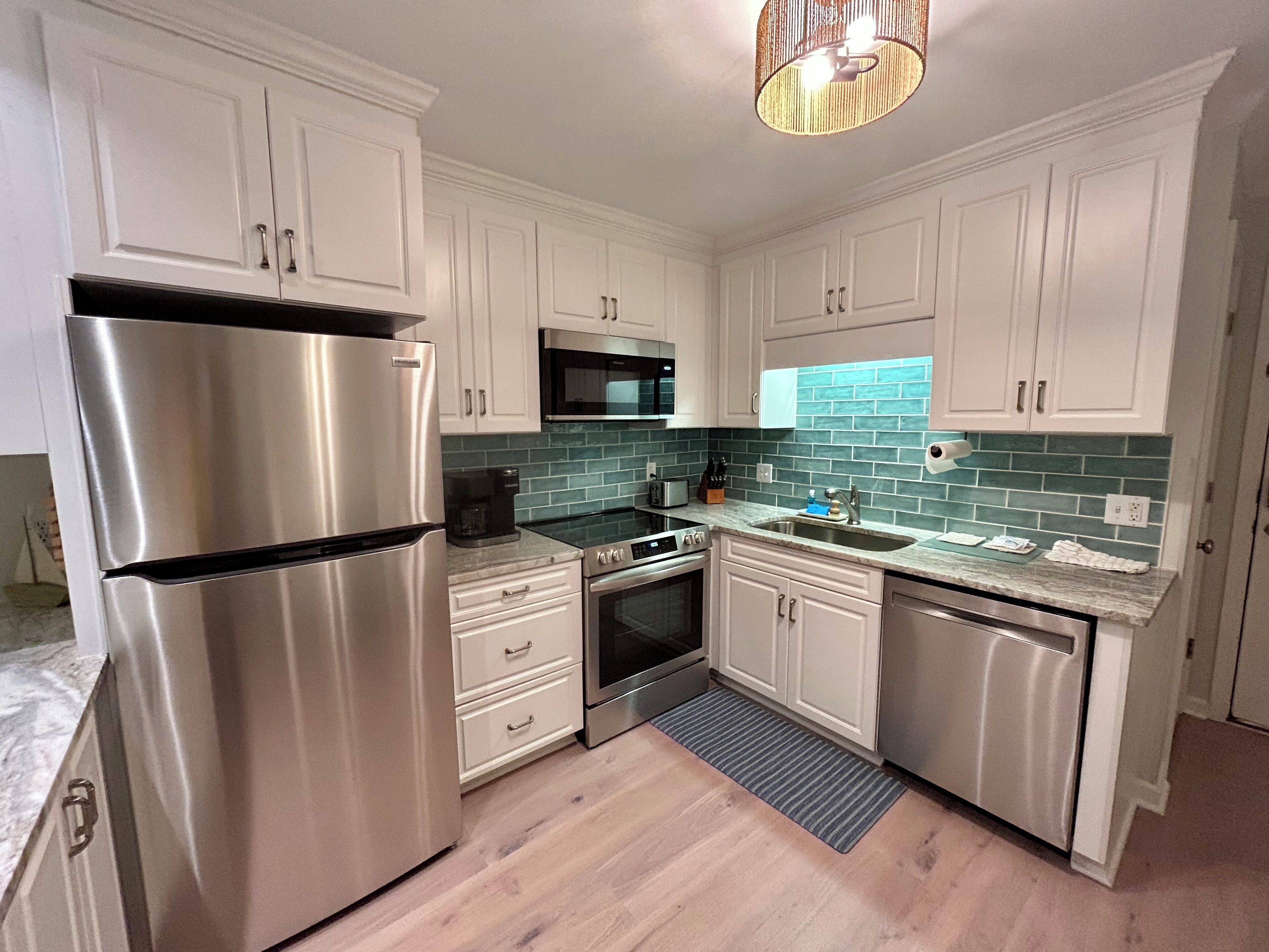 Una cocina moderna con armarios blancos, electrodomésticos de acero inoxidable, un microondas y salpicadero con azulejos verdes.