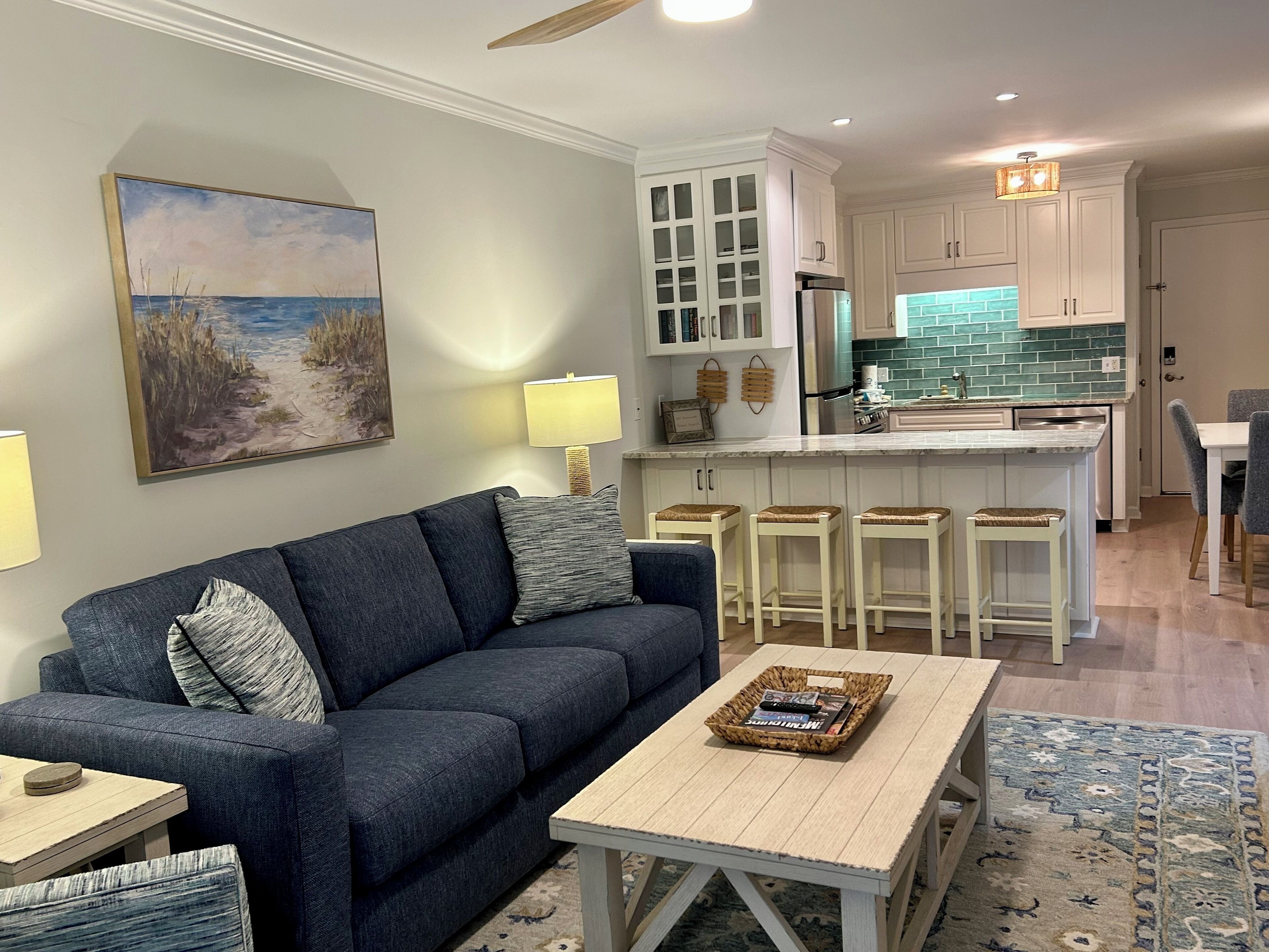 A modern living room with a dark blue sofa, a coffee table, and a painting of a beach scene.