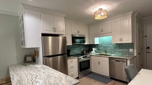 A modern kitchen with white cabinets, stainless steel appliances, a marble countertop, and a green-tiled backsplash.