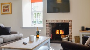 Una sala de estar con chimenea, un sofá, una mesa de centro con una botella y vasos, y un televisor montado en la pared.