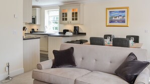 Sala de estar con sofá, mesa de comedor con sillas, área de cocina con armarios y fregadero, y un cuadro en la pared.