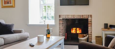 A living room with a fireplace, a sofa, a coffee table with a bottle and glasses, and a TV mounted on the wall.