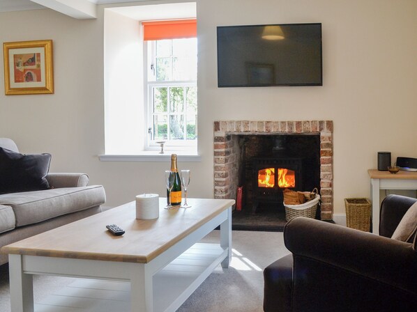 A living room with a fireplace, a sofa, a coffee table with a bottle and glasses, and a TV mounted on the wall.