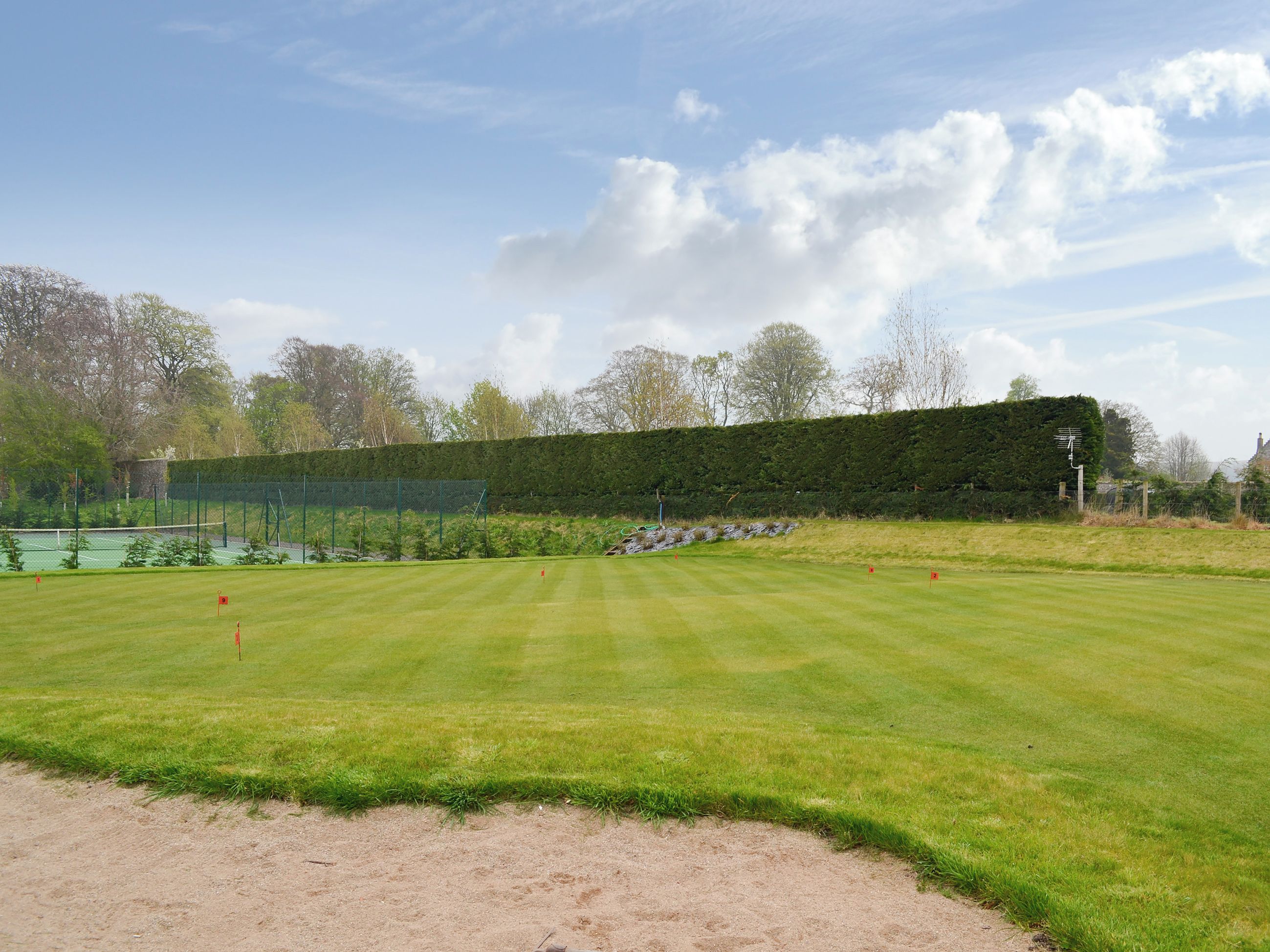 A well-maintained golf course with a clear sky, neatly trimmed grass, and a hedge in the background.