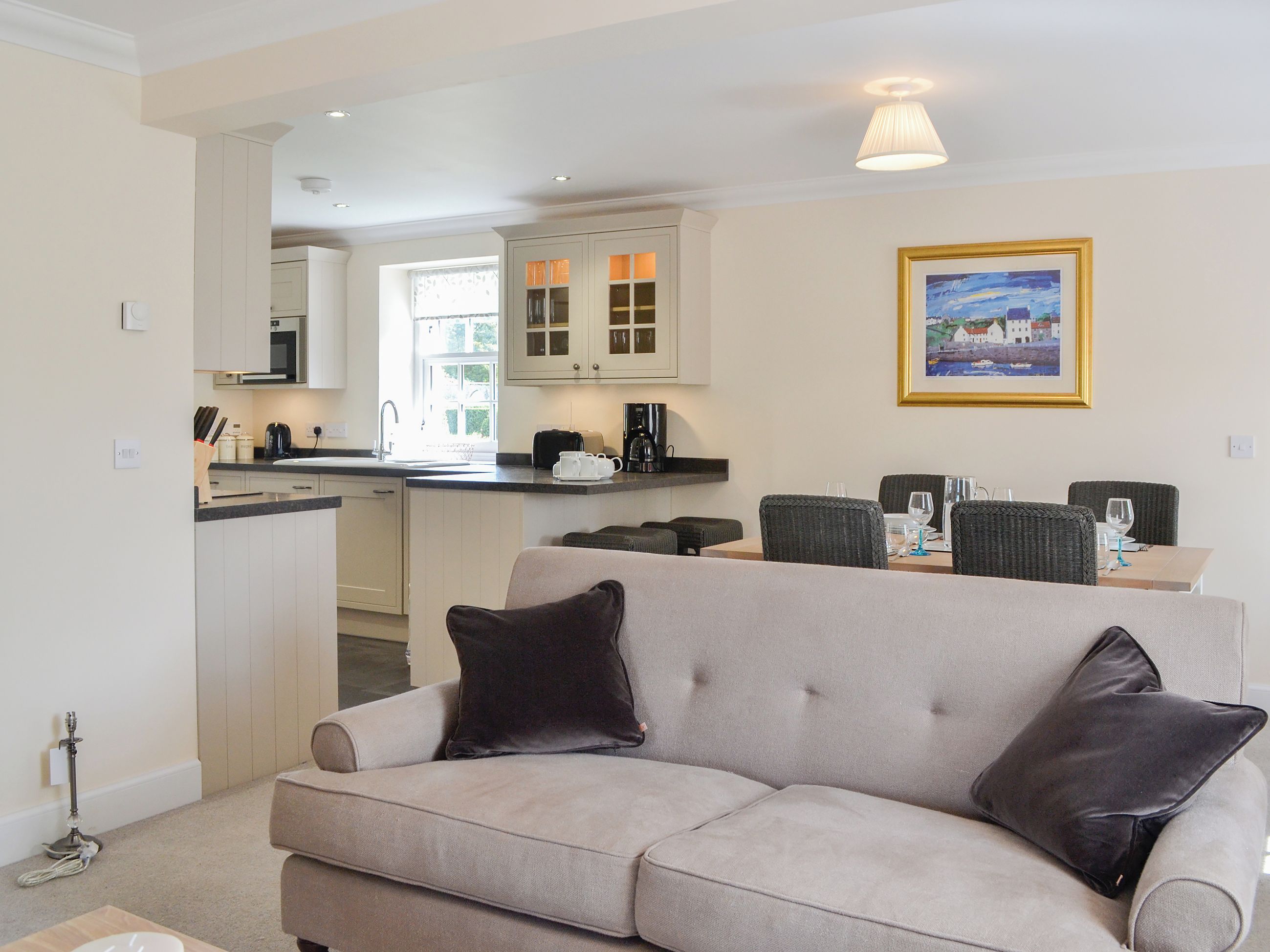 A living room with a sofa, a dining table with chairs, a kitchen area with cabinets and a sink, and a framed picture on the wall.