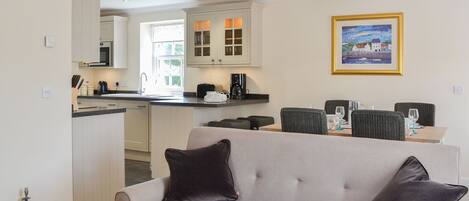 A living room with a sofa, a dining table with chairs, a kitchen area with cabinets and a sink, and a framed picture on the wall.