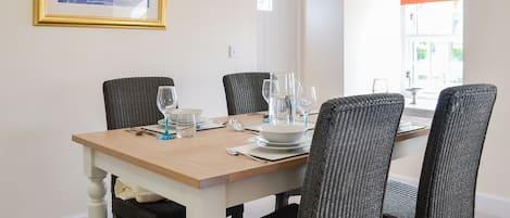 A dining table with four chairs, a framed painting, and a window with blinds.
