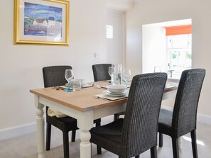 Een eettafel met vier stoelen, een lijst met een schilderij en een raam met zonwering.