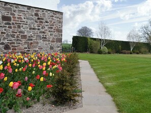 A stone building with a garden of tulips and a grassy lawn.