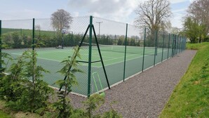 A tennis court with a green fence, trees, and a clear sky. - Grieve's Cottage - UK11107 (Montrose)