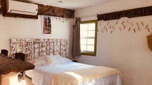Une chambre à coucher comprenant un lit, une tête de lit en bois, une fenêtre avec des rideaux et un appareil de climatisation fixé au mur.