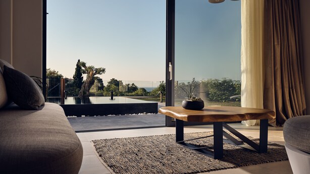 Un salon moderne doté d’une grande porte-fenêtre coulissante donnant sur un balcon, d’une table basse en bois et offrant une vue sur la verdure et un plan d’eau.