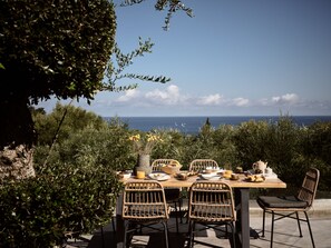 An outdoor dining area with wicker chairs and a table set for a meal, overlooking a scenic ocean view. - Alexandros Deluxe SeaView Villa, with Heated Pool (Zakynthos)