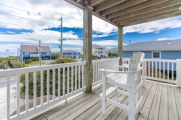 A wooden deck with a white railing, overlooking a residential area with houses and a clear sky.