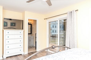Ein Schlafzimmer mit einem Bett, einer Kommode, einer Schiebetür zu einem Balkon und einem Deckenventilator.