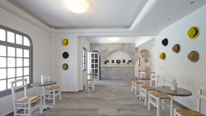A dining area with white chairs and tables, a stone fireplace, and a view through an arched doorway. - Crystal Palace (Santorini)