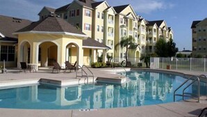 A swimming pool with lounge chairs and a covered seating area, surrounded by multi-story buildings with balconies. - Cane Island (Kissimmee)