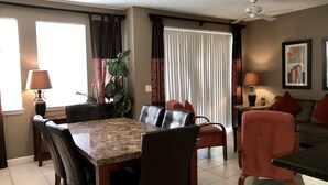 A dining area with a table and chairs, a sofa, a ceiling fan, and a window with curtains. - Cane Island (Kissimmee)