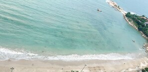 A beach with clear turquoise water, a sandy shore, and a rocky outcrop with vegetation. - Cala Bayview Muong Thanh (Bac Nha Trang)