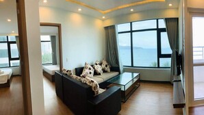 A modern living room with a sofa, a glass coffee table, and a large window offering a view of the sea. - Cala Bayview Muong Thanh (Bac Nha Trang)