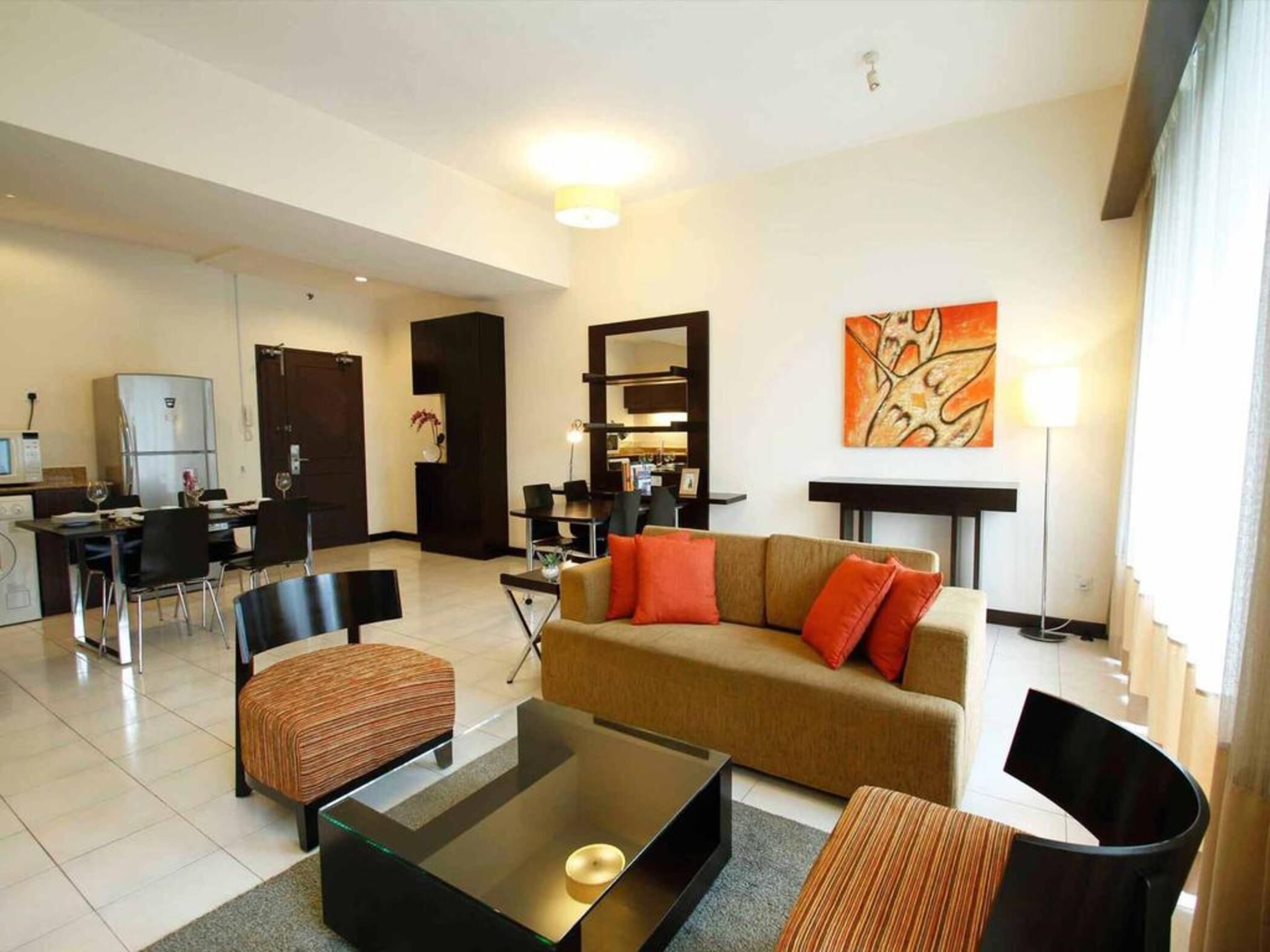 A modern living room with a sofa, chairs, a coffee table, a dining area with chairs, a kitchen area, and a painting on the wall.