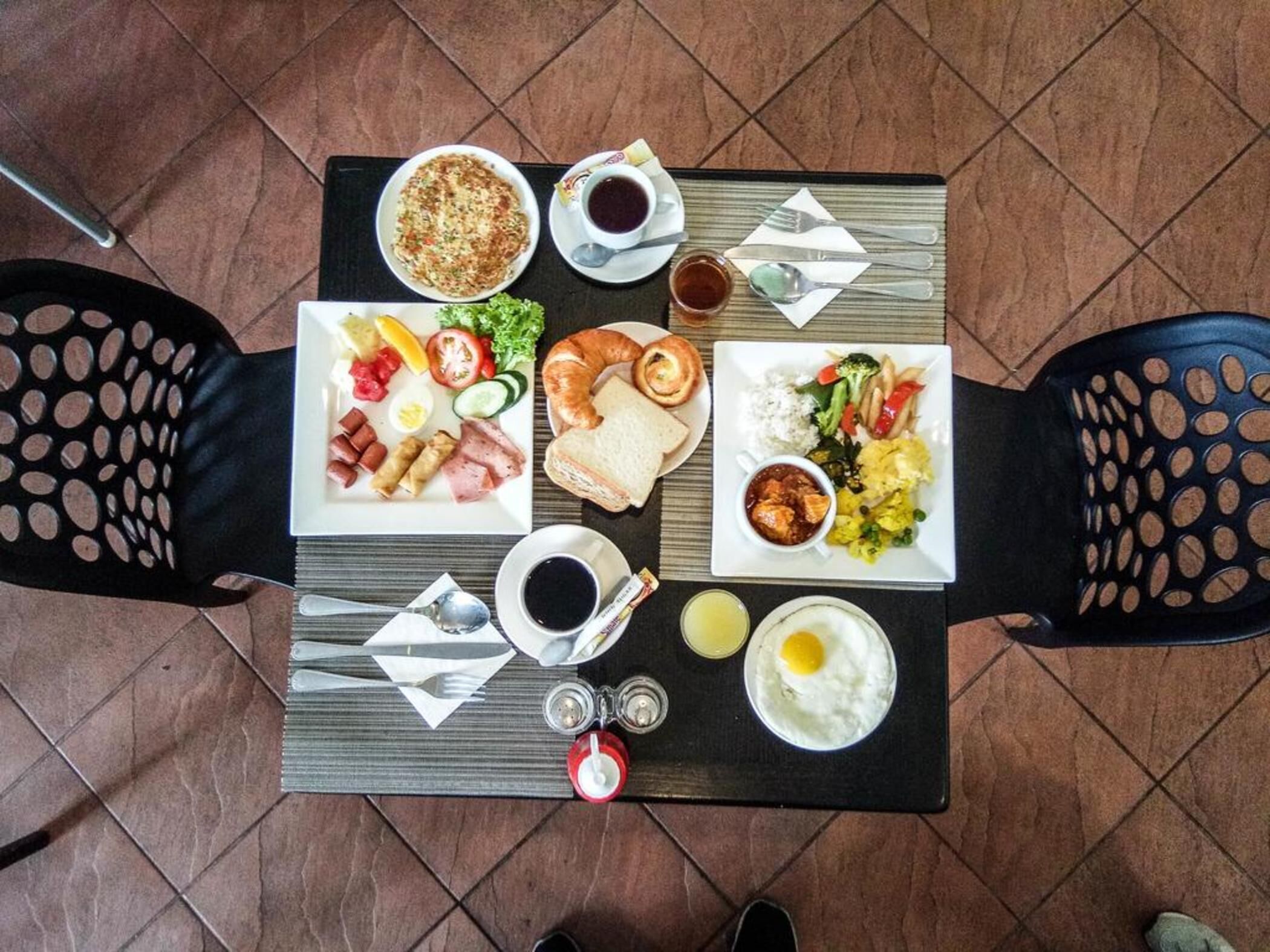 Una mesa de desayuno con platos de comida, tazas y cubiertos.