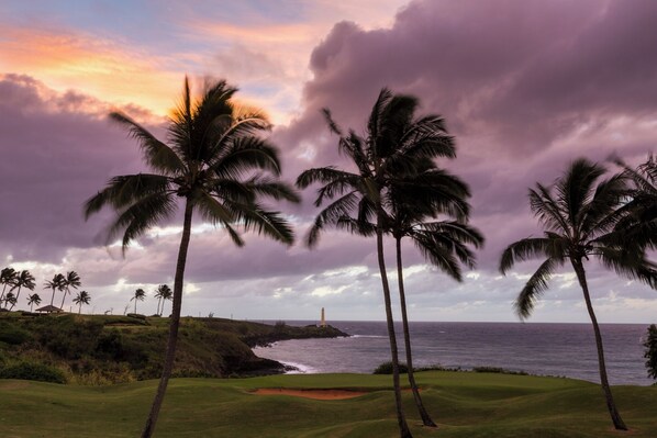 A golf course with palm trees and a lighthouse in the distance.