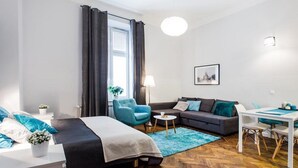 A modern hotel room with a bed, a sofa, a dining table, and a small side table. - Apartamenty Pod Wawelem Wroblewskiego (Kraków)
