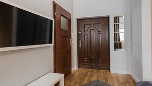 A hallway with a wooden door, a white bench, and a window with blinds. - Apartamenty Pod Wawelem Wroblewskiego (Kraków)