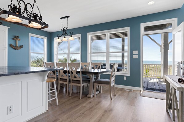 A kitchen with a dining area, wooden chairs, a marble countertop, and a view of the ocean through large windows.
