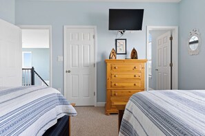 A bedroom with two beds, a dresser, a TV, and a door leading to a balcony. - Pirate`s Booty by Brunswick Vacation Rentals: OIB 5BR Oceanfront Home w/ Pool (Ocean Isle Beach)