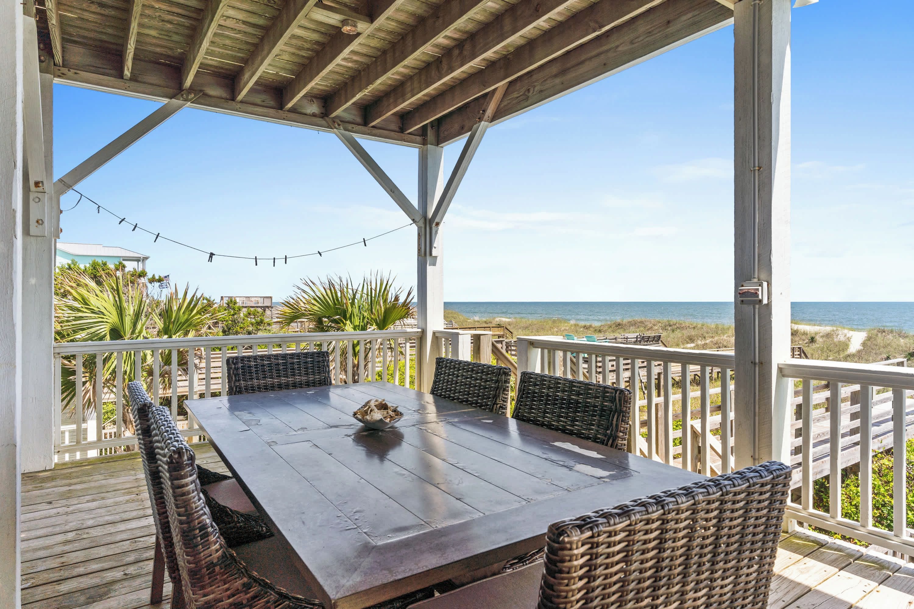 A covered outdoor seating area with a table and chairs, overlooking a beach.