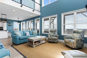 A spacious living room with a high ceiling, large windows, and nautical-themed decor.