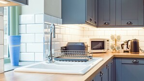 Une cuisine moderne équipée d’un évier, d’un égouttoir, d’un four à micro-ondes et d’une bouilloire posés sur le plan de travail.