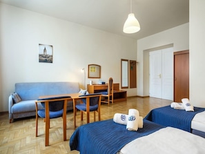 Une chambre d’hôtel avec un canapé, un bureau, deux lits, un miroir et un tableau au mur.