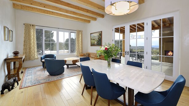 A spacious dining area with a large table and blue chairs, a wooden ceiling, and a view of the outdoors through large windows. - 3 Bedroom, 3 Bath Home plus 1 Bedroom, 1 Bath Casita -12 min. to Santa Fe center (Santa Fe)